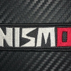 May include: A black embroidered patch with the white text "NISMO" and a red square with a white "O" inside.