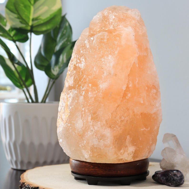 May include: A large, natural Himalayan salt lamp with a warm orange glow. The lamp is on a wooden base with a black cord.