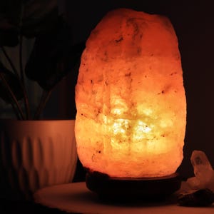 May include: A warm, orange-toned Himalayan salt lamp with a wooden base. The lamp is lit and glowing, casting a soft light.