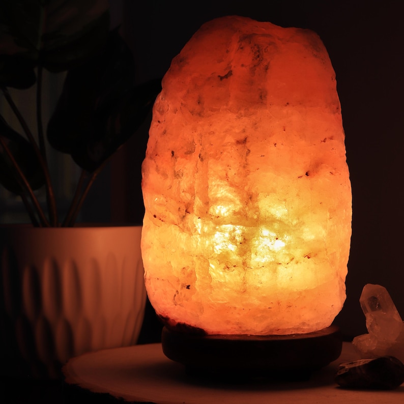 May include: A warm, orange-toned Himalayan salt lamp with a wooden base. The lamp is lit and glowing, casting a soft light.