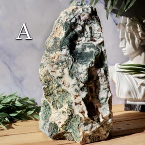 May include: A large, rough-hewn stone with a mix of green, white, and tan colors. The stone has a natural, organic shape and texture. The letter "A" is visible in the upper left corner. The stone is likely a decorative item or a natural specimen.
