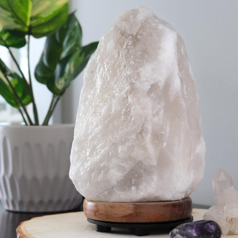 May include: A large, white Himalayan salt lamp with a wooden base. The lamp is sitting on a wooden surface.