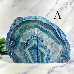 May include: Two blue agate bookends with a natural, layered pattern. The bookends are cut from a single stone, displaying concentric bands of blue, white, and gray. The letter "A" is visible in the upper right corner.