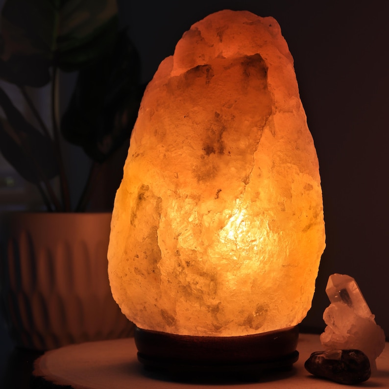 May include: A large, irregularly shaped Himalayan salt lamp with a warm, orange glow. The lamp is sitting on a wooden base and is illuminated from within.