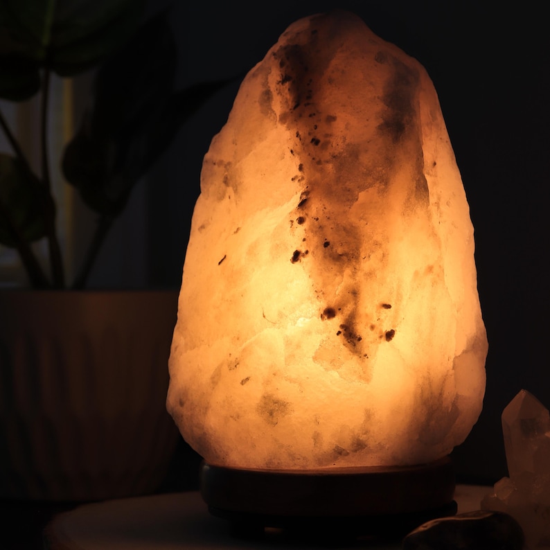 May include: A large, white Himalayan salt lamp with a warm, orange glow. The lamp is made from a natural crystal and has a wooden base.