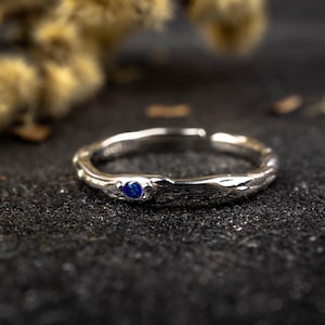 Könnte beinhalten: Ein silberner Ring mit einem strukturierten, astähnlichen Design und einem einzigen blauen Edelstein.