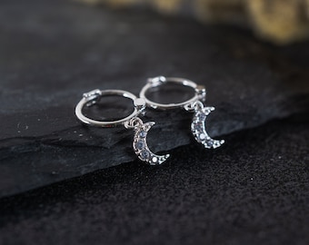 May include: A pair of silver hoop earrings with a crescent moon charm. Each moon charm is adorned with small, clear crystals.