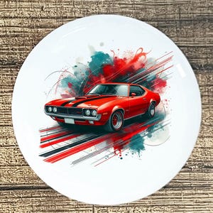 May include: White ceramic plate featuring a red classic car with black racing stripes. The car is set against a backdrop of red, teal, and black abstract paint strokes. The plate has a glossy finish.