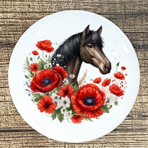 May include: A white, round decorative plate featuring a horse's head surrounded by red poppies and white flowers. The horse has a dark brown coat and black mane. The poppies have a dark blue center.