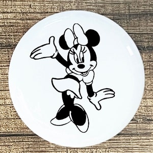 May include: Black and white illustration of Minnie Mouse waving with a big smile. She is wearing a dress and her signature bow.