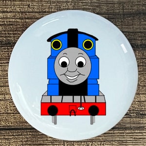 May include: A blue and red cartoon train engine with a smiling face and black wheels. The train has yellow headlights and a black stripe down the middle.