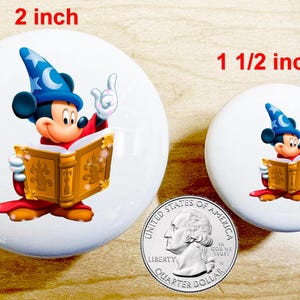 May include: Two white, round buttons featuring Mickey Mouse in a sorcerer's outfit, reading a book. The larger button is 2 inches in diameter, and the smaller one is 1 1/2 inches. A US quarter is included for size comparison.