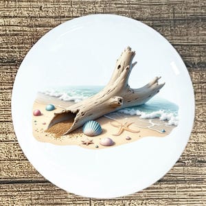 May include: White ceramic plate featuring a beach scene. A weathered driftwood log rests on a sandy shore with seashells and starfish. The ocean waves are visible in the background, creating a coastal theme.