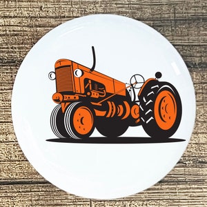 May include: Orange and black tractor illustration on a white round sticker.