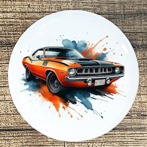 May include: A ceramic plate featuring a classic orange and black muscle car design. The car is depicted with watercolor-style splashes of orange and blue. The plate has a white background and a glossy finish.