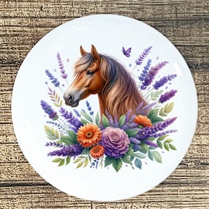 May include: A white, round decorative plate featuring a horse's head surrounded by purple lavender, orange and purple flowers, and green leaves. A purple butterfly is also present. The horse has a brown coat and flowing mane.