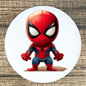 May include: A white ceramic plate featuring a cartoon illustration of Spider-Man. The character is depicted in his classic red and blue suit with a black spider emblem on the chest. The plate has a glossy finish.
