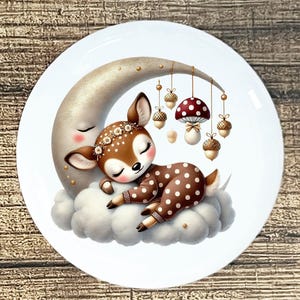 May include: A decorative plate featuring a sleeping fawn with a floral crown, resting on a cloud next to a crescent moon. The fawn wears a brown and white polka-dot outfit. Hanging from the moon are acorns and a mushroom.