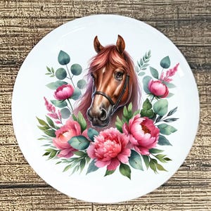 May include: White round plate featuring a watercolor illustration of a horse's head with a bridle, surrounded by pink peonies, green leaves, and eucalyptus. The horse has a brown coat and pink mane.
