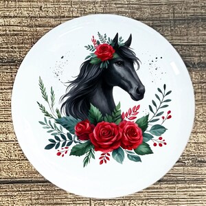 May include: White ceramic plate featuring a black horse head adorned with a red rose crown and a bouquet of red roses and green leaves. The horse has flowing black hair. The plate has a glossy finish.