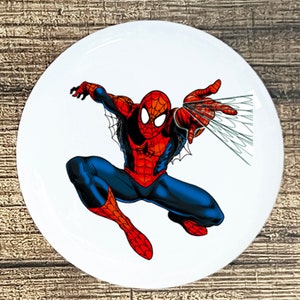 May include: A red and blue superhero, Spiderman, is swinging through the air with a web shooter in his right hand. He is wearing a red and blue suit with a spider logo on his chest.