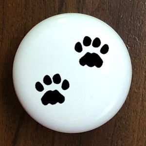 May include: White ceramic round ornament with two black paw prints.