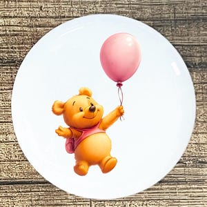May include: A round, white plate featuring a cartoon bear holding a pink balloon. The bear is wearing a pink shirt and backpack. The image has a whimsical, cheerful design, perfect for children's decor.