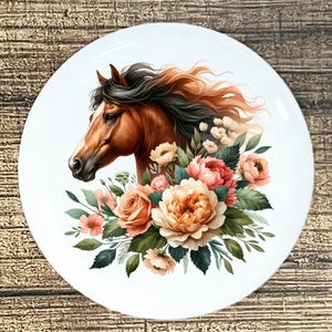 May include: White ceramic plate featuring a detailed illustration of a horse's head with flowing mane, surrounded by a bouquet of pink, peach, and cream-colored flowers and green foliage. The horse has a brown coat and a white stripe on its face.