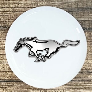 May include: A white round sticker with a silver and black running horse logo. The horse is facing left and has a long flowing mane.