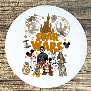 May include: White ceramic plate featuring a "Star Wars" design with iconic characters like Darth Vader, Mickey Mouse, and Donald Duck. The plate includes the "Star Wars" logo and space-themed graphics.
