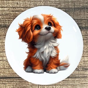 Puede incluir: Un plato de cerámica blanco con una pintura digital de un cachorro Cavalier King Charles Spaniel. El cachorro tiene pelaje naranja y blanco, ojos negros grandes y mira hacia arriba. El plato tiene un acabado brillante y está sobre un fondo de madera.