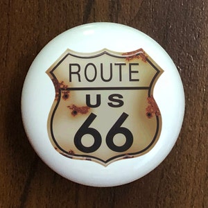May include: A white ceramic round ornament with a rusty Route US 66 sign printed on it.