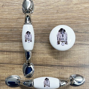 May include: Three ceramic cabinet knobs with a silver finish. Each knob features a white background with a printed image of the Star Wars character R2-D2.