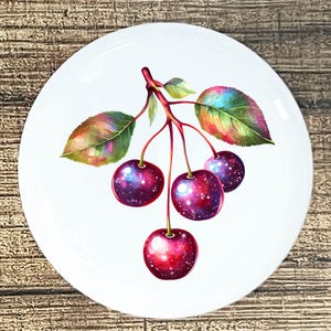 May include: White ceramic plate featuring a vibrant illustration of cherries. The cherries are a deep red with a galaxy-like pattern, and the leaves have a colorful, iridescent effect. The plate is round and has a glossy finish.