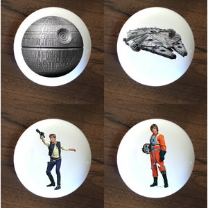 May include: Four white ceramic round knobs with Star Wars themed images. The top left knob features the Death Star, the top right knob features the Millennium Falcon, the bottom left knob features Han Solo, and the bottom right knob features Luke Skywalker.