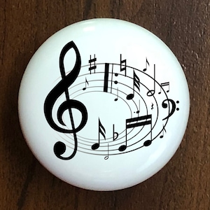 May include: White ceramic tile with a black treble clef and musical notes. The notes are arranged in a circle around the treble clef.