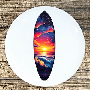 May include: A decorative surfboard featuring a sunset scene with a vibrant orange and red sky, a bright yellow sun, and blue ocean waves. The surfboard is set against a white background.