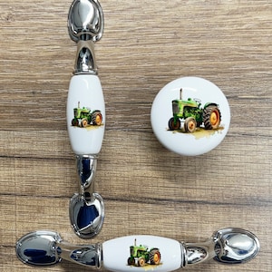 May include: Three ceramic cabinet knobs with a green tractor design. The knobs are white with a silver metal base. The tractor is green and yellow with black wheels.