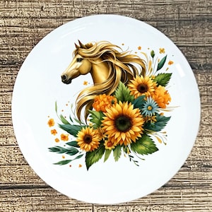 May include: White ceramic plate featuring a golden horse head with flowing mane, surrounded by sunflowers, orange flowers, and green leaves. The design is centered on the plate, creating a decorative and artistic piece.