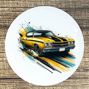May include: A white ceramic plate featuring a yellow classic car with black racing stripes. The car is depicted in motion with artistic streaks of yellow, black, and blue. The car has the letters "SS" on the front.