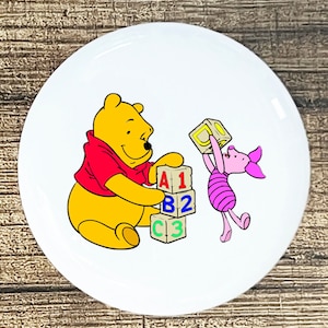 May include: Winnie the Pooh and Piglet are playing with colorful alphabet blocks. The blocks spell out "A1 B2 C3".