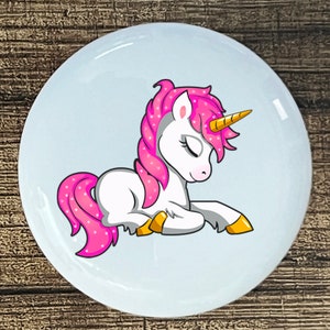 May include: A white unicorn with pink glitter mane and tail is lying down with its eyes closed. The unicorn has a gold horn and hooves.