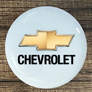 May include: A white round button with a gold Chevrolet logo and the word "CHEVROLET" in black text.