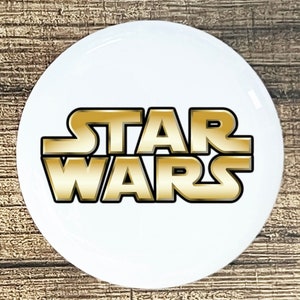 May include: A white round button with the gold text "STAR WARS" on it.