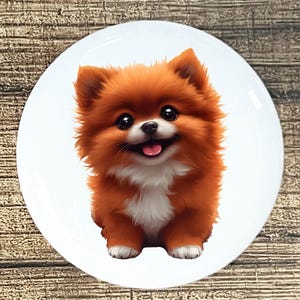 May include: A round white plate featuring a cartoon illustration of a Pomeranian dog. The dog has fluffy orange fur, a white chest, and a pink tongue. The dog is smiling with big black eyes.