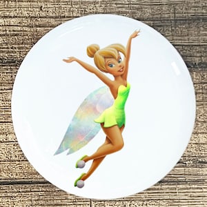 May include: A round sticker featuring Tinker Bell, a Disney fairy with blonde hair, green wings, and a green dress. She is flying with her arms outstretched.