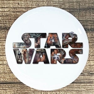 May include: A white round button with the word "STAR WARS" in black letters. The letters are made up of images from the Star Wars movies.