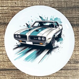 May include: White ceramic plate featuring a vintage car illustration. The car is white with teal racing stripes and accents, and the word "Pontiac" is visible. Teal paint splatters and stylized birds add to the design.