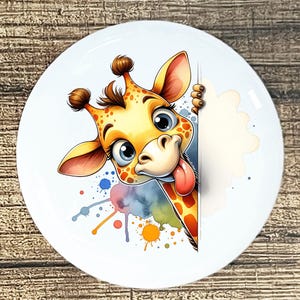 May include: A white ceramic plate featuring a cartoon giraffe with a playful expression. The giraffe has a yellow and orange coat with brown spots, big blue eyes, and its tongue sticking out. Colorful paint splatters add a whimsical touch.