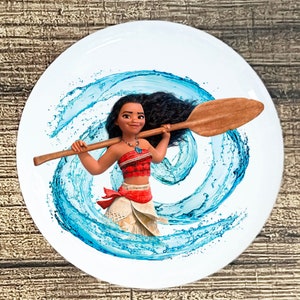 May include: A white ceramic plate with a colorful image of a cartoon character holding a wooden paddle. The character has long black hair, brown eyes, and is wearing a red and white top and a brown skirt. The background is a blue swirl pattern.